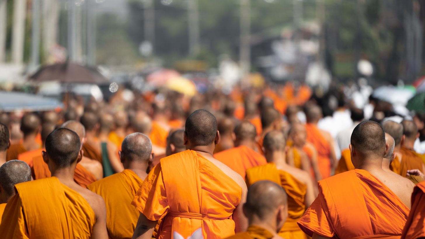 A large procession of Buddhist monks in saffron robes walking along a street