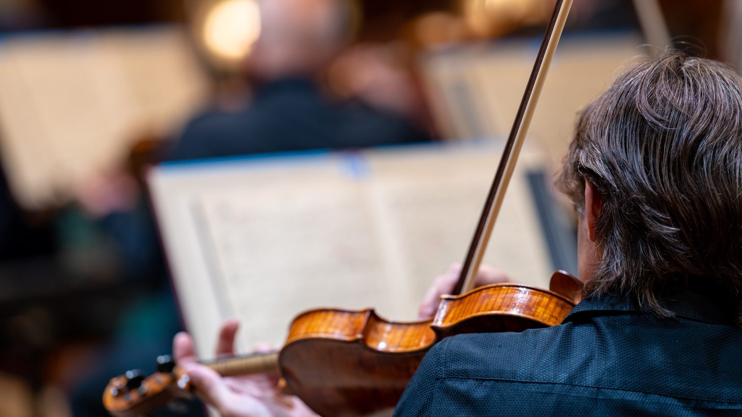 Violinists playing from shared sheet music during an orchestral performance