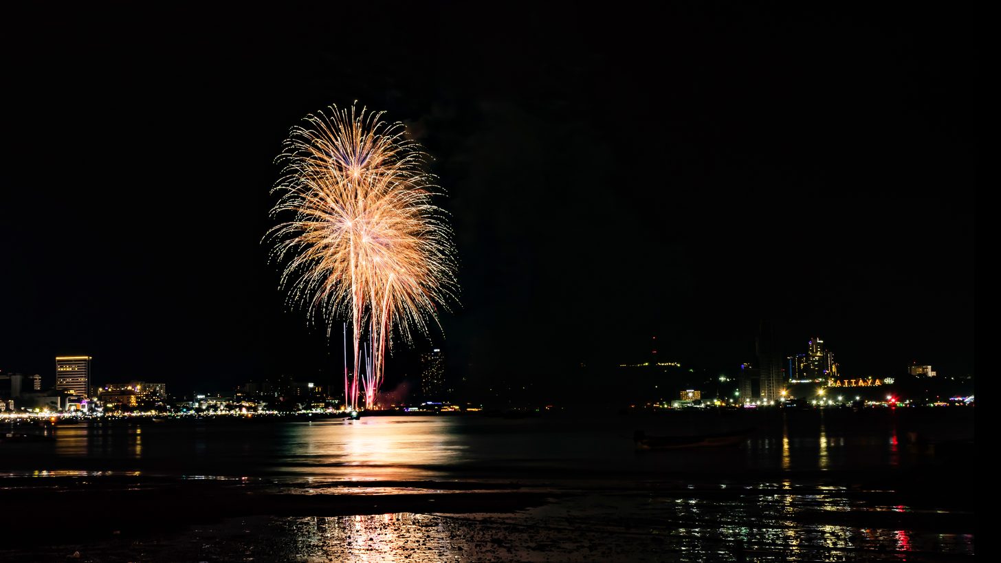 A firework burst over Pattaya bay at night with the lit hillside sign beyond