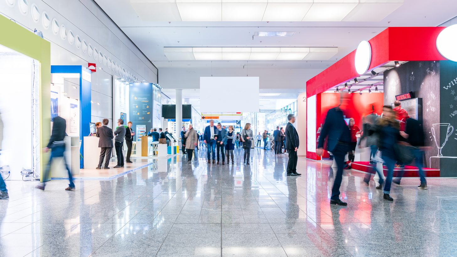 Visitors walking between exhibition stands in a large convention hall