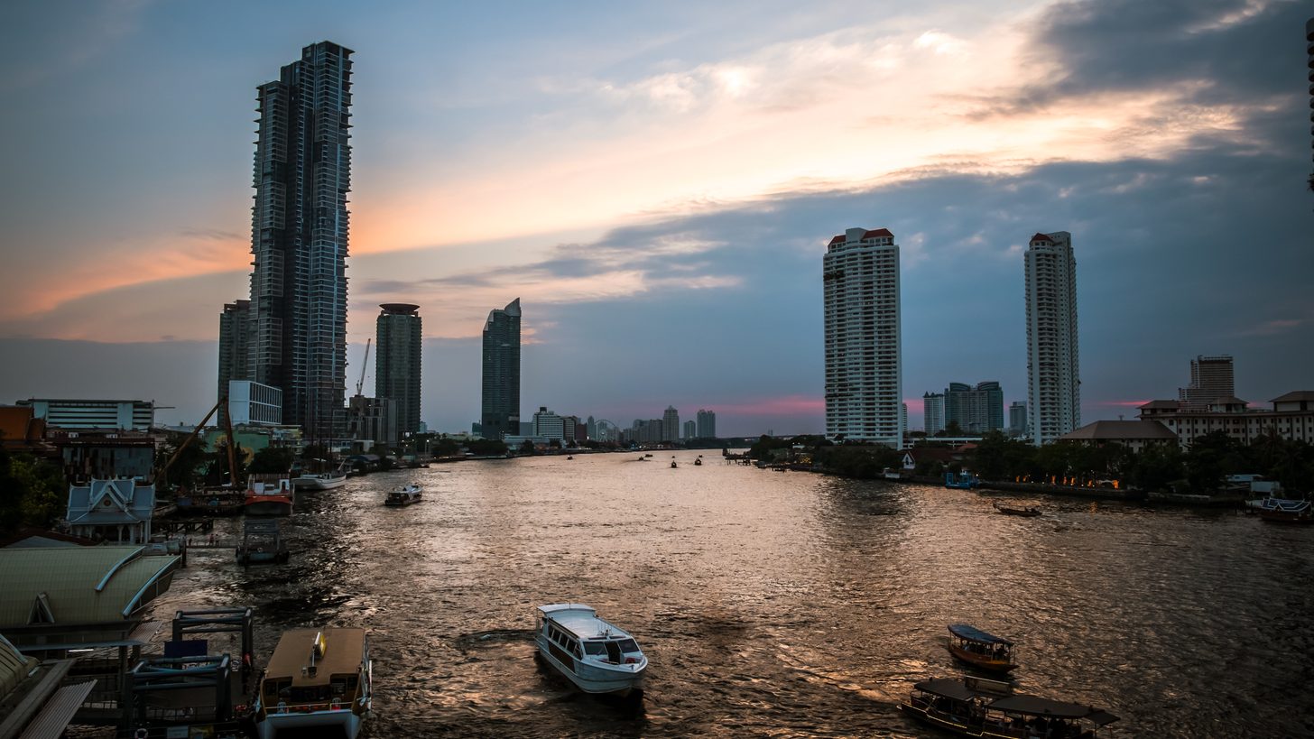 The Chao Phraya at sunset with riverside towers, piers and passenger boats