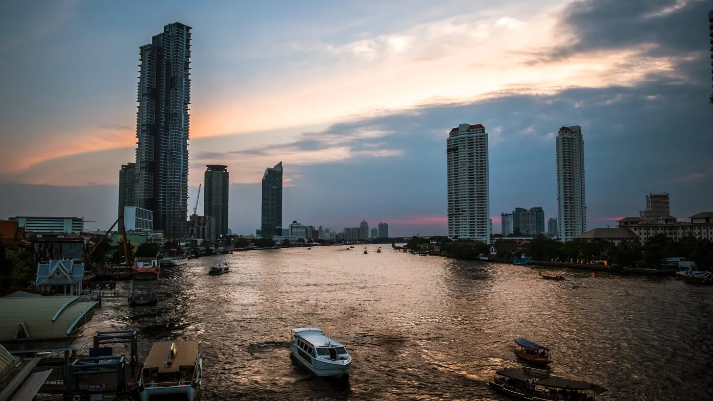Der Chao Phraya bei Sonnenuntergang, mit Türmen, Anlegern und Passagierbooten am Ufer