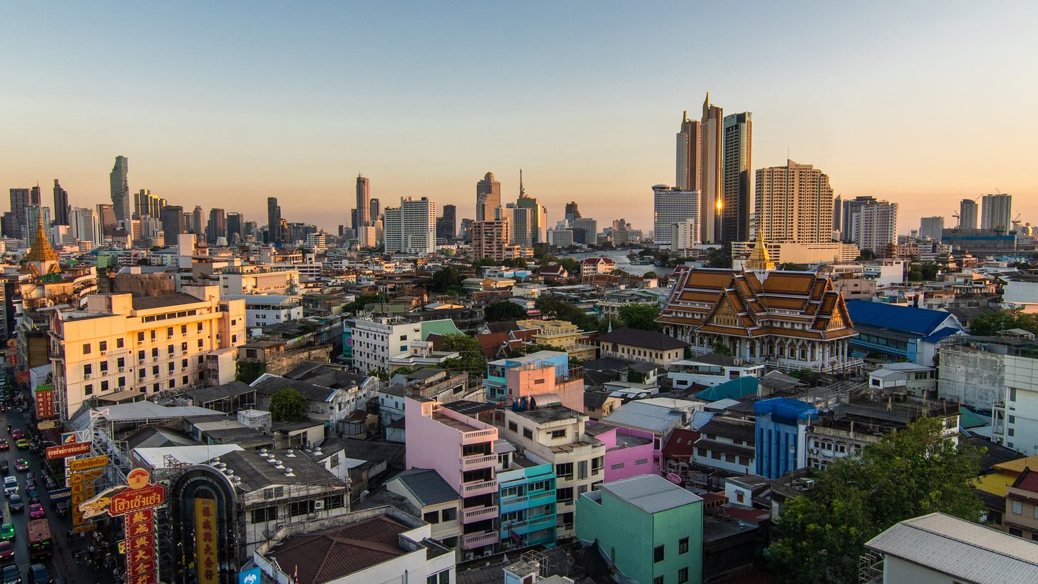 Bangkok's low-rise riverside quarters seen from above at golden hour, with the business district towers behind