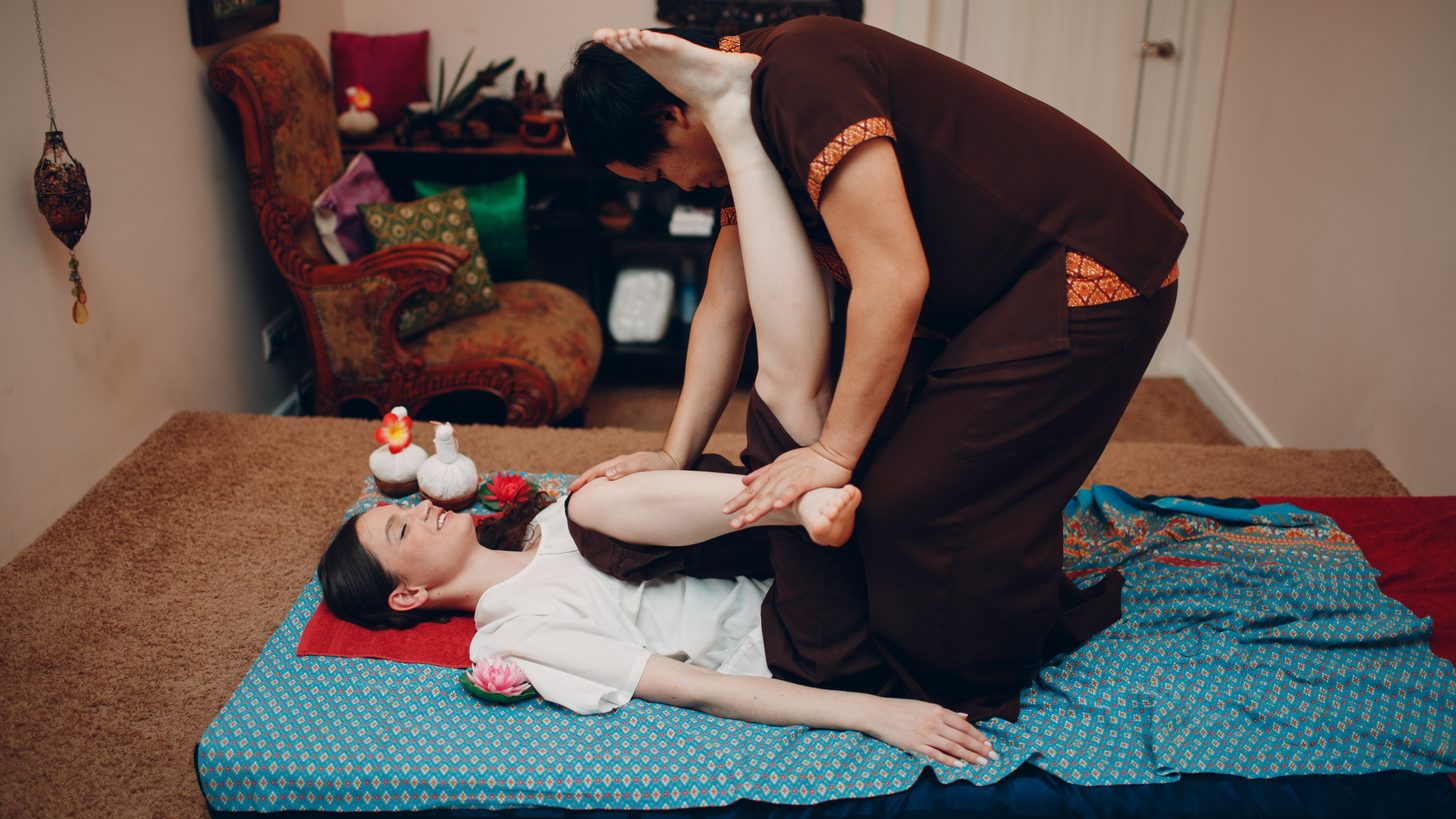 A therapist performing a traditional Thai massage stretch on a floor mat in a treatment room