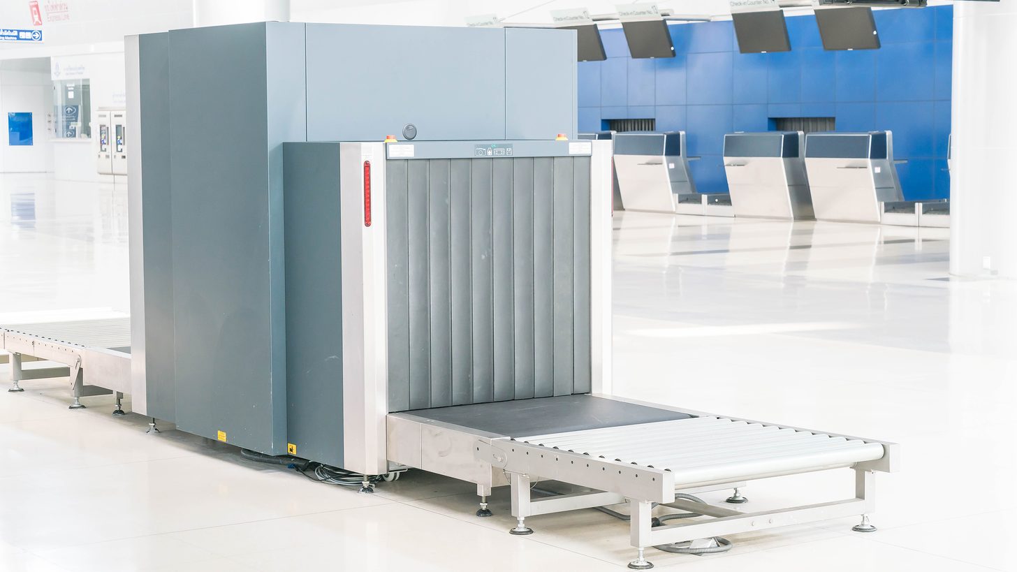 A hold-baggage x-ray screening machine beside check-in counters in an airport terminal