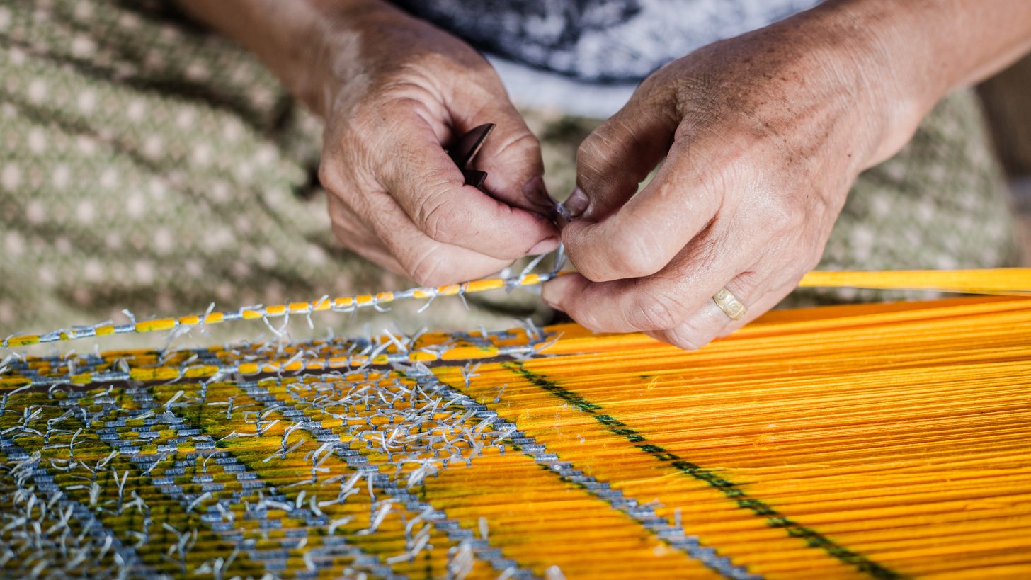 Hands working a traditional silk weaving loom with coloured thread