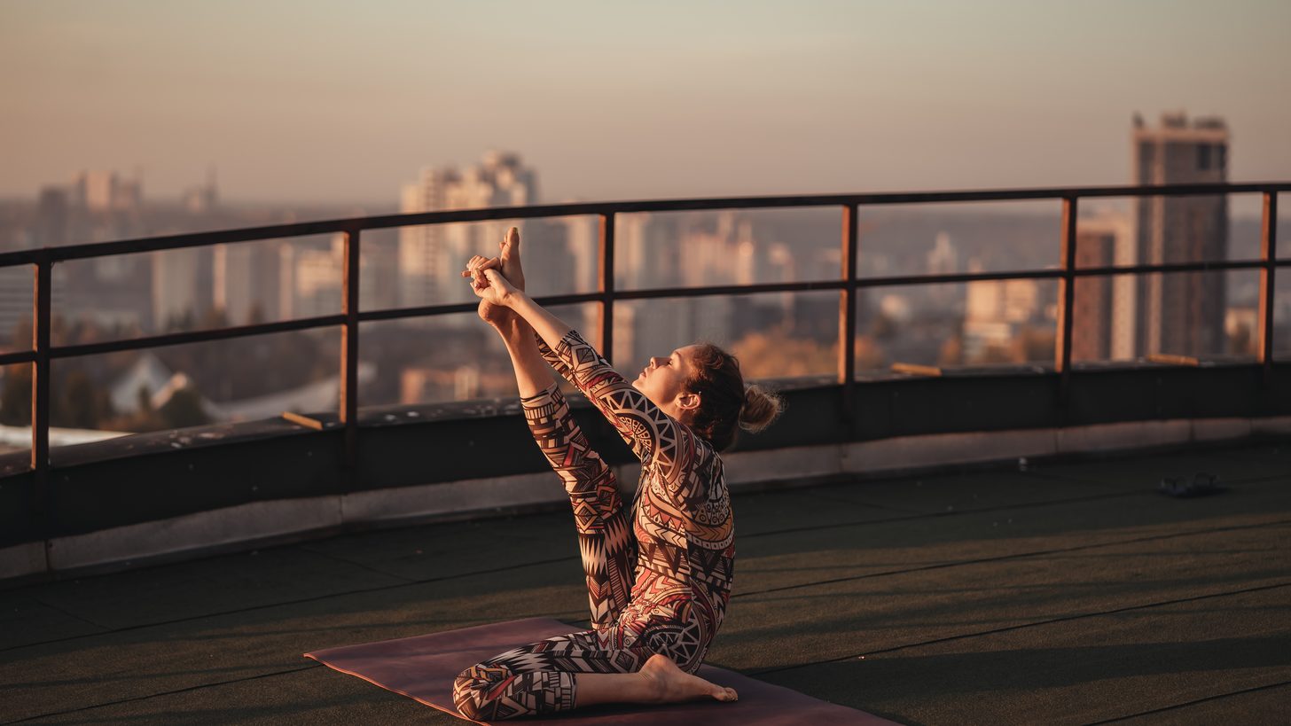 A person practising yoga on a rooftop terrace above a city skyline at dusk