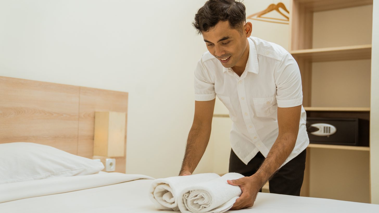 A hotel room attendant placing rolled towels on a made bed