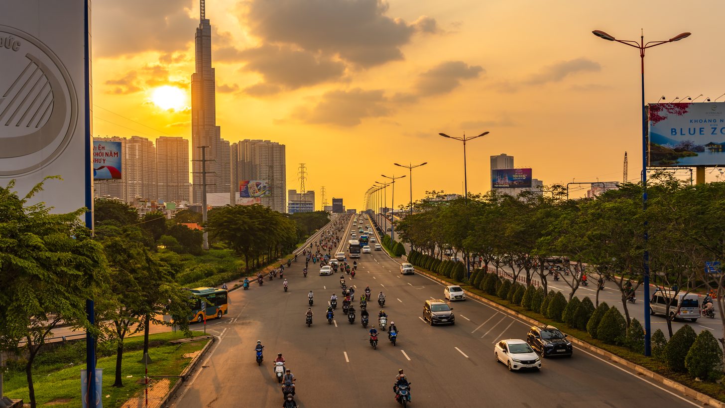 Evening traffic on a Ho Chi Minh City boulevard with the Landmark 81 tower against a golden sky
