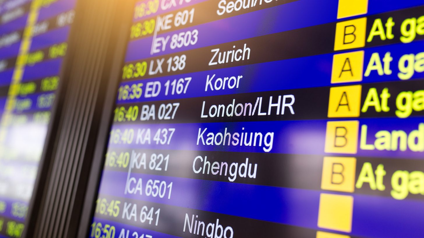 A departures board in an airport terminal listing flight numbers, destinations and gates