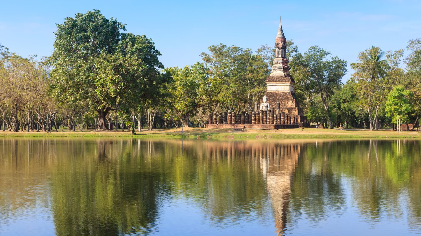 Stupa and seated Buddha of Sukhothai Historical Park reflected in still water