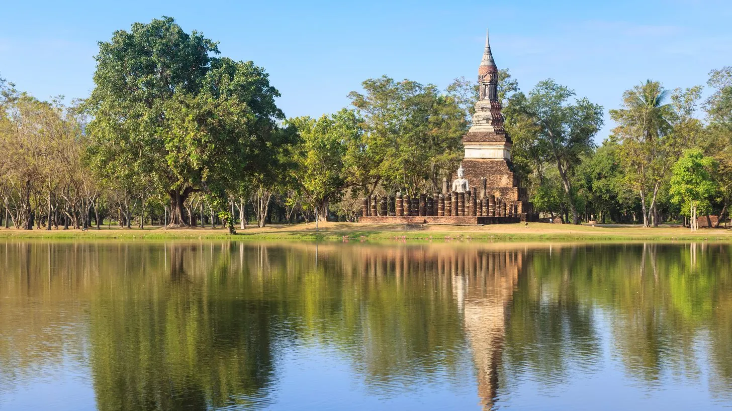 Stupa und sitzender Buddha im Geschichtspark Sukhothai, gespiegelt in stillem Wasser