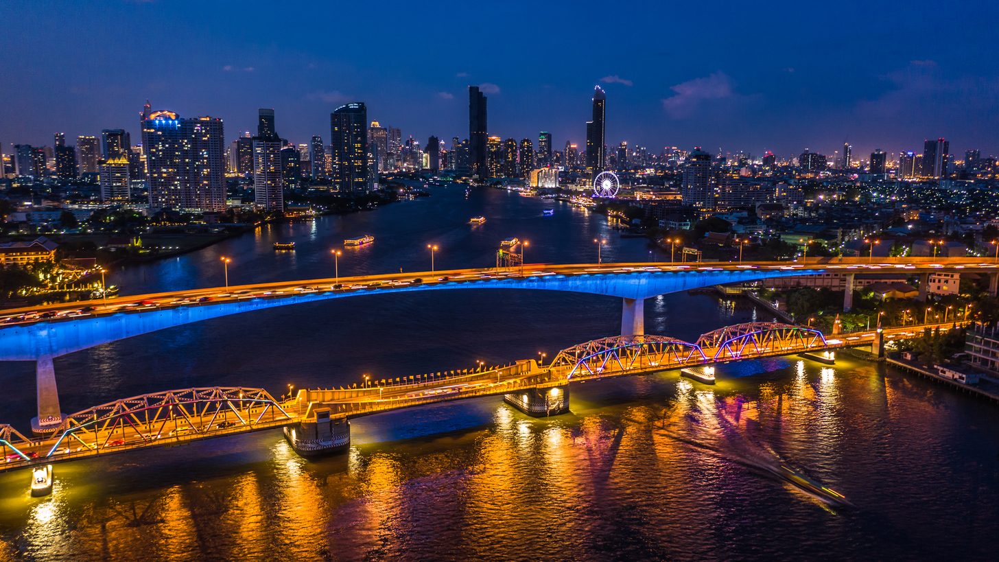 Aerial view of the Bangkok skyline at night with the Chao Phraya River winding through the lit downtown