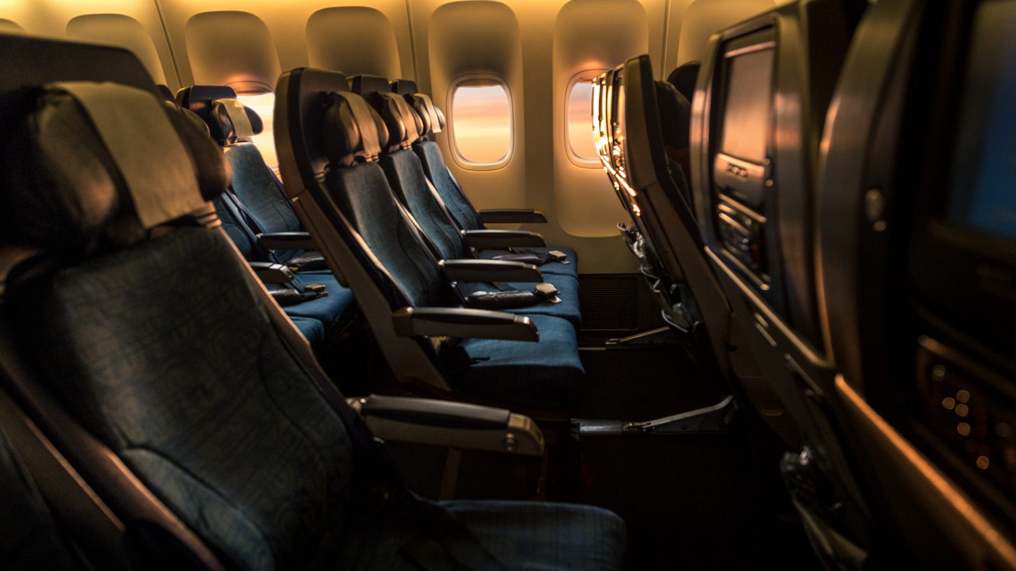 Rows of seats in a twin-aisle airliner cabin with sunset light through the windows
