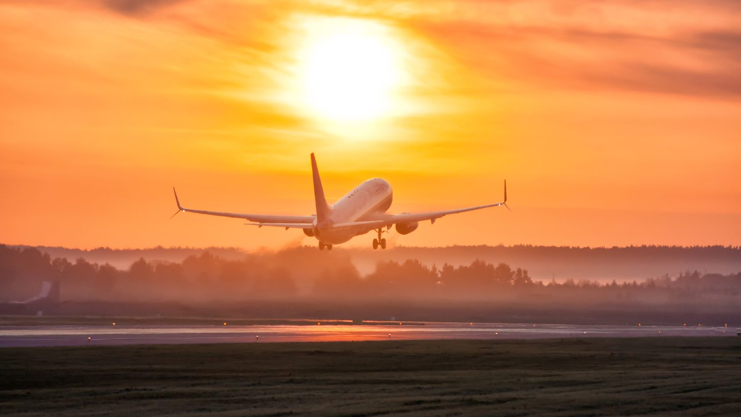 An airliner lifting off from a runway at dawn through low mist