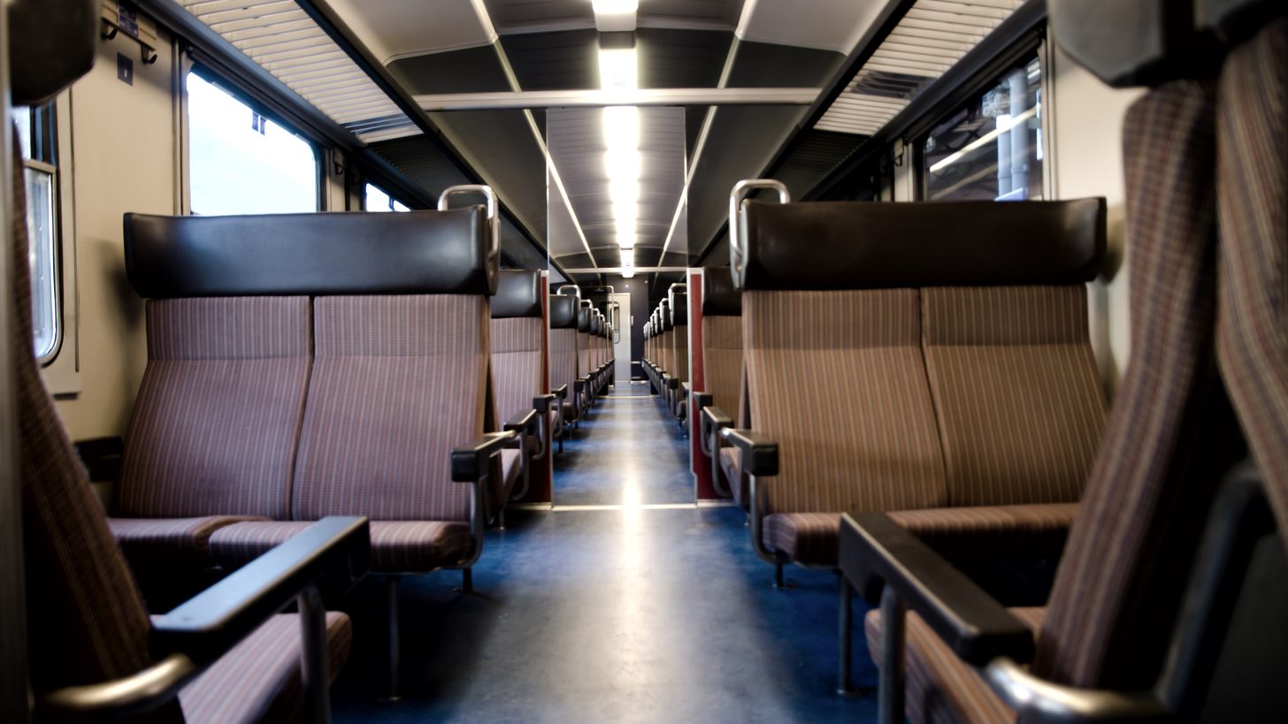 The aisle of an empty commuter railcar lined with unreserved bench seats