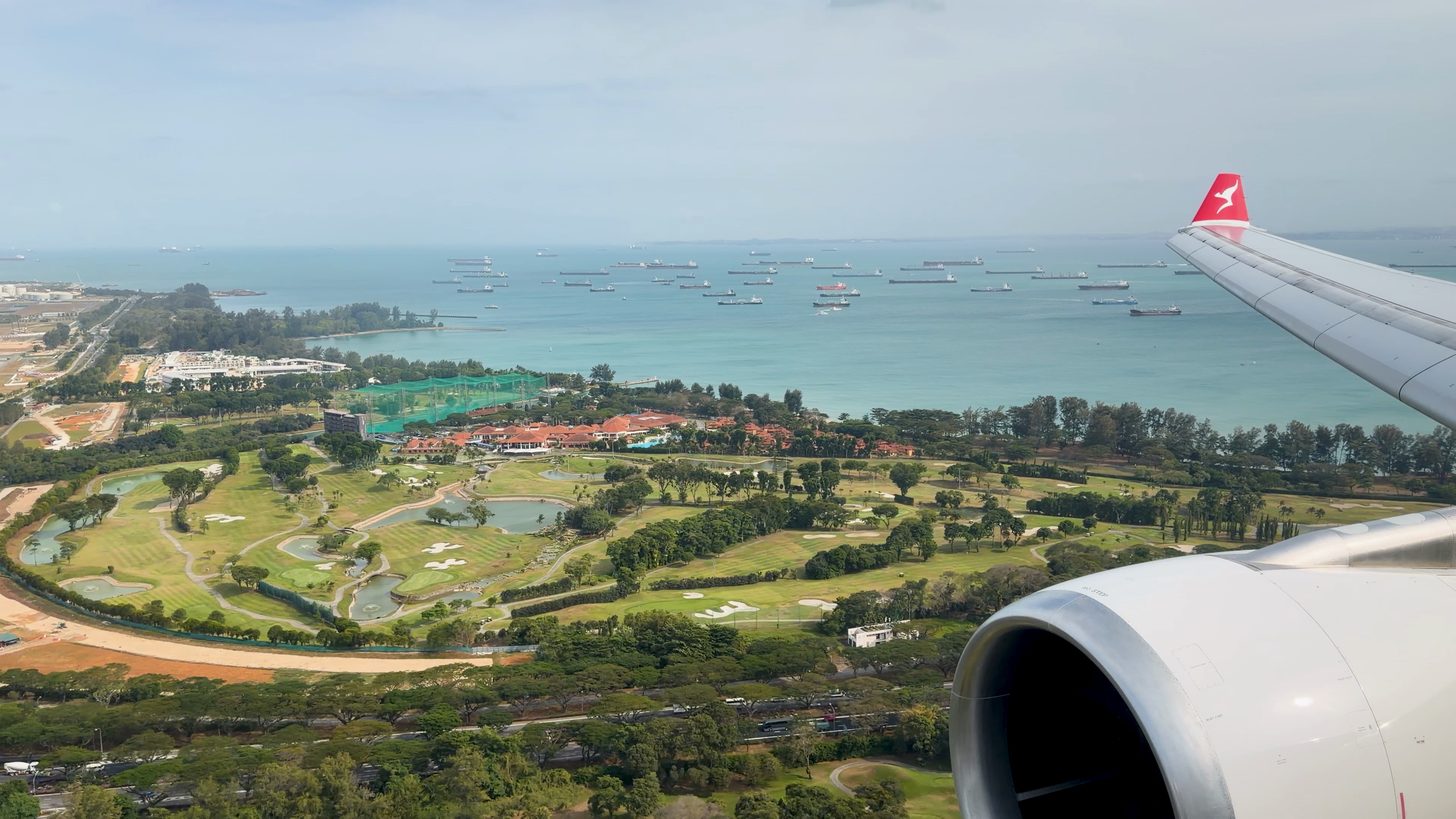 A window view on approach over the Singapore coast, with cargo ships anchored offshore and the aircraft wing in frame