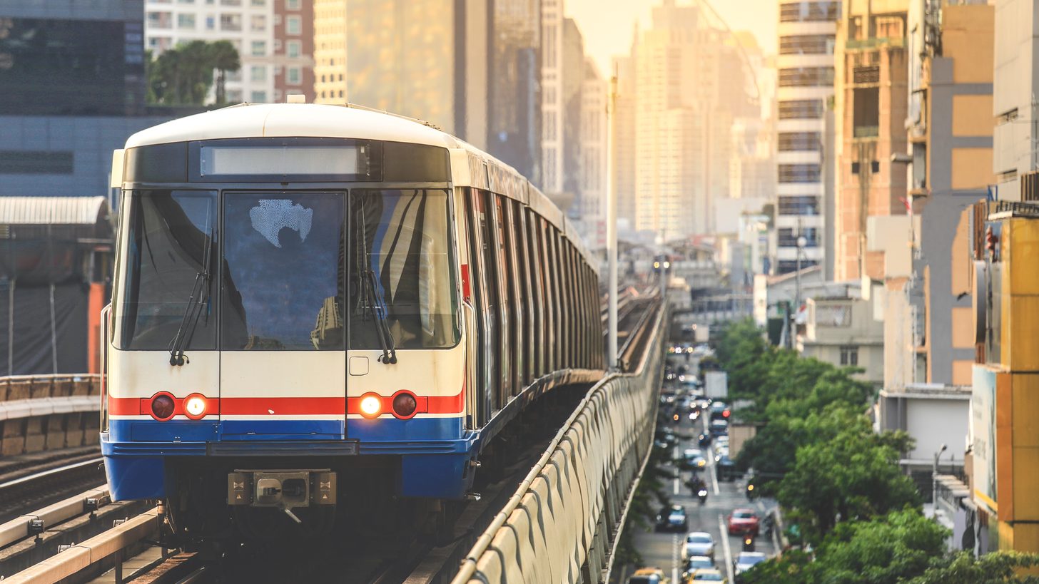 A BTS Skytrain running on its elevated track above a congested Bangkok street at golden hour