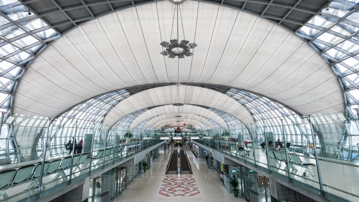 The long curved concourse of Suvarnabhumi Airport's main terminal, seen from an upper level, with a moving walkway running down the centre