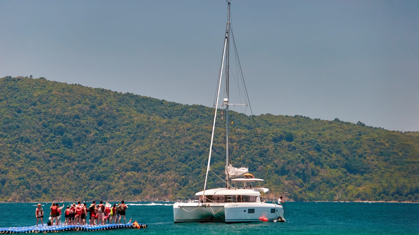 A group of travellers on a floating jetty beside a moored catamaran