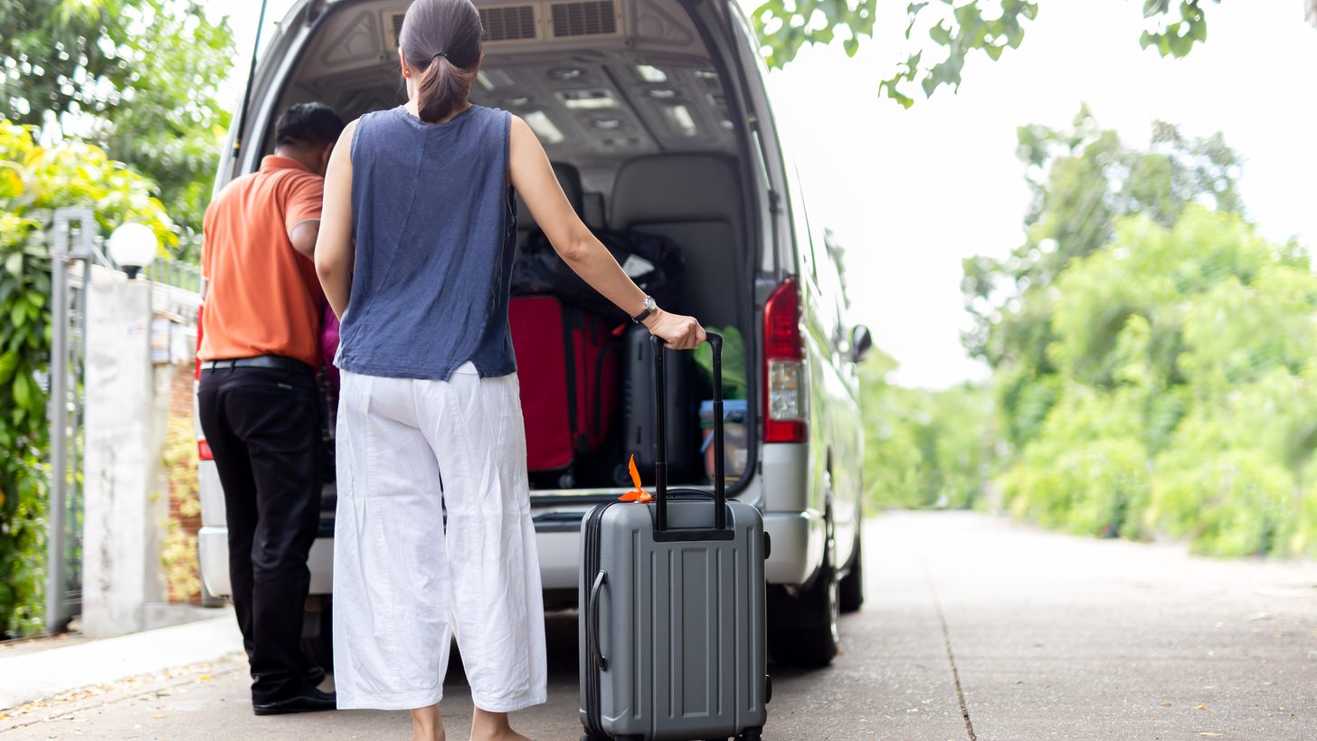 A driver loading a traveller's luggage into a minibus