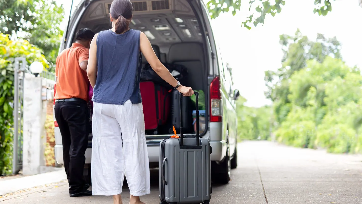 Ein Fahrer lädt das Gepäck eines Reisenden in einen Minibus