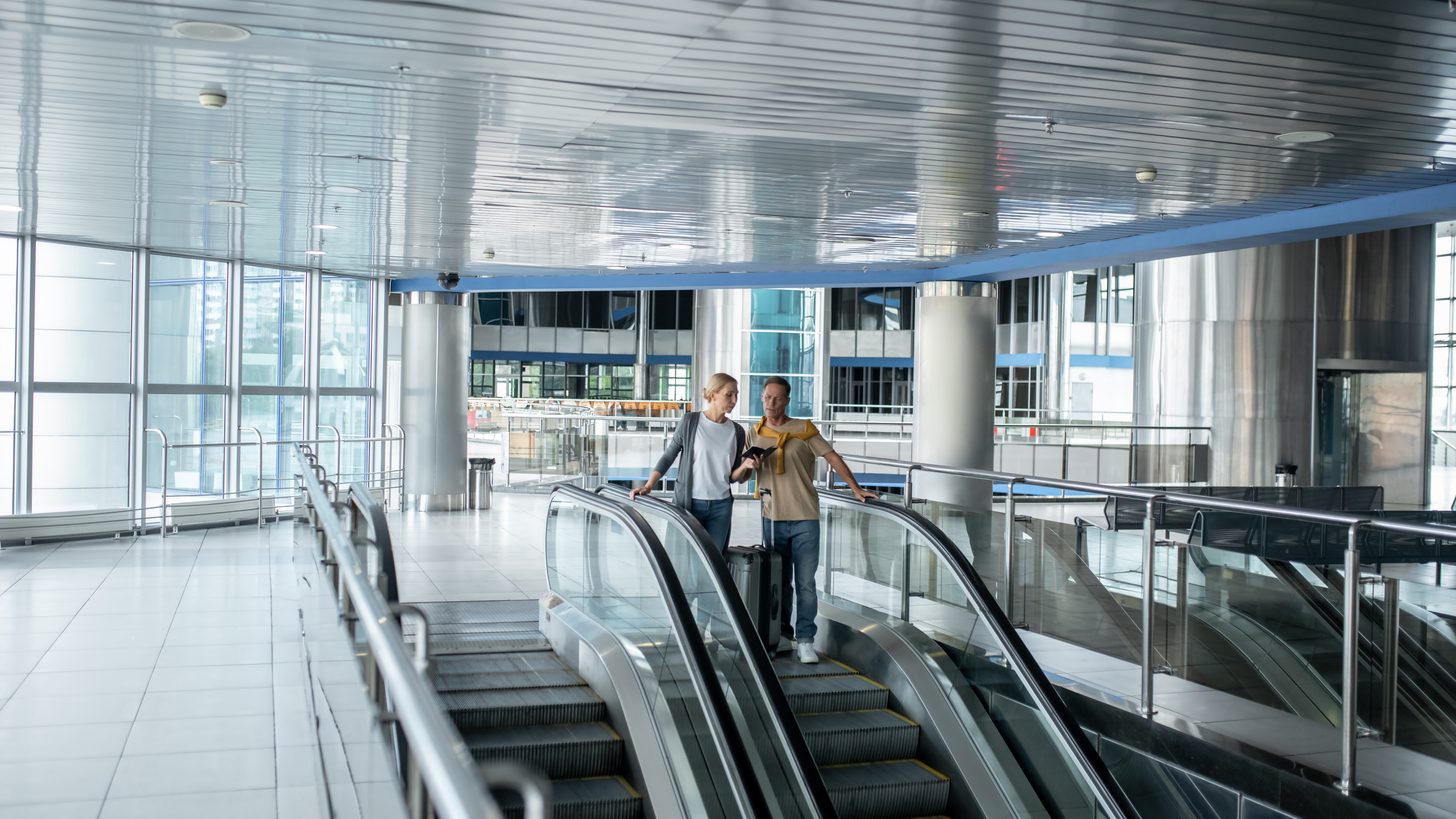 Two travellers checking a travel document while riding an airport escalator