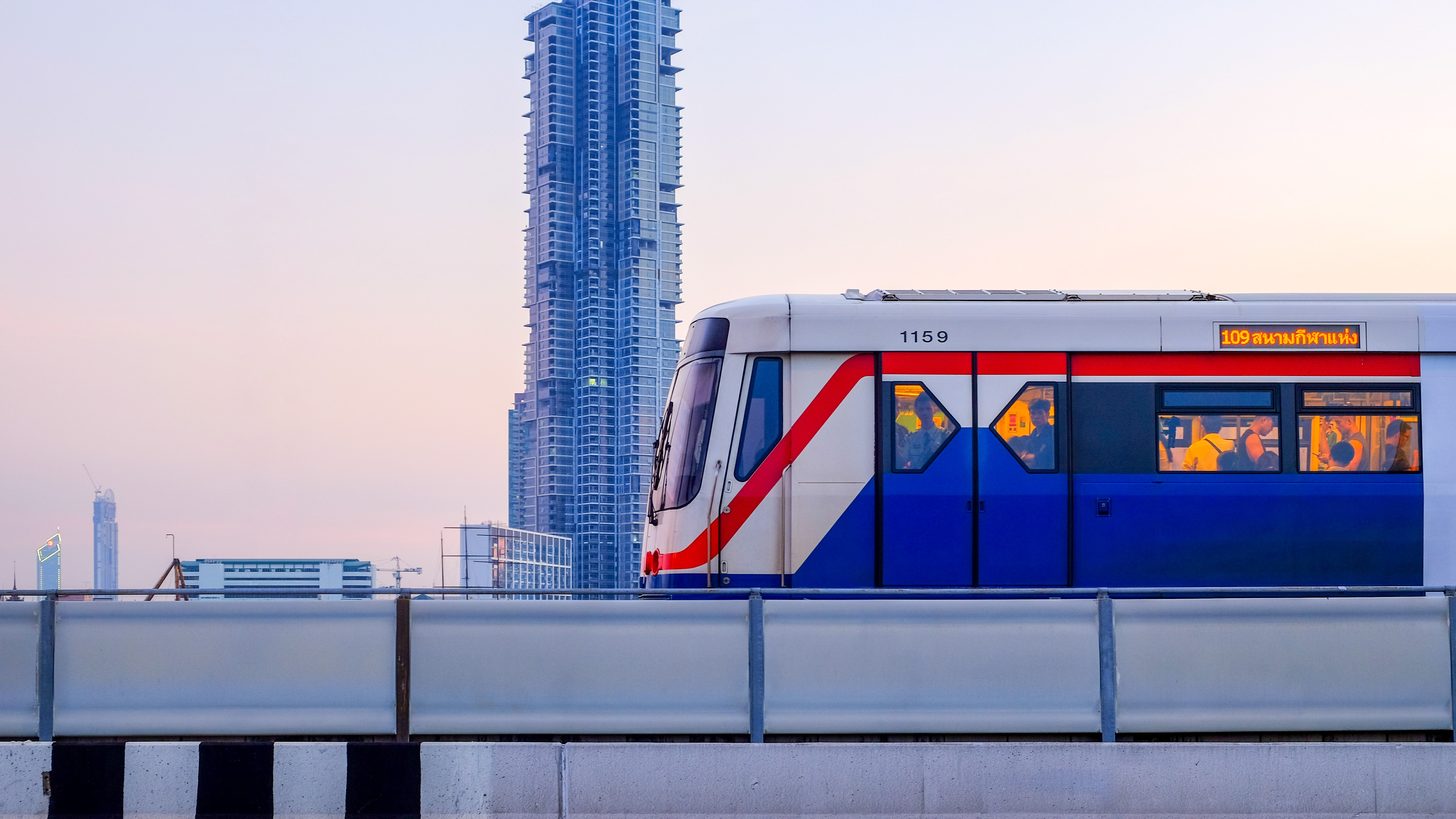 Ein BTS Skytrain überquert das Zentrum Bangkoks in der Dämmerung, dahinter Hochhaustürme