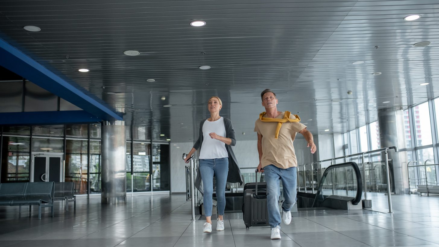 Two passengers with rolling luggage hurrying along an airport terminal