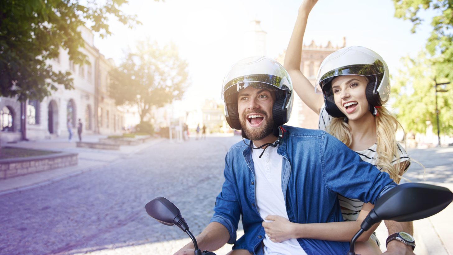 A couple wearing helmets riding a rented motorbike along a tropical road