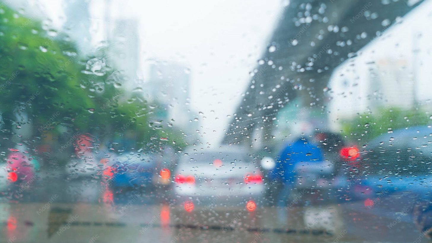 Rain on a car windscreen in slow city traffic, the part of an airport run that decides whether a client makes the flight