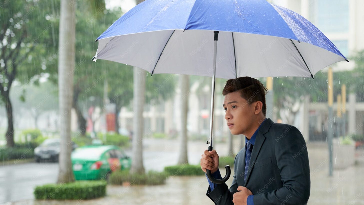 A traveller under an umbrella waiting for a taxi on a rain-soaked street