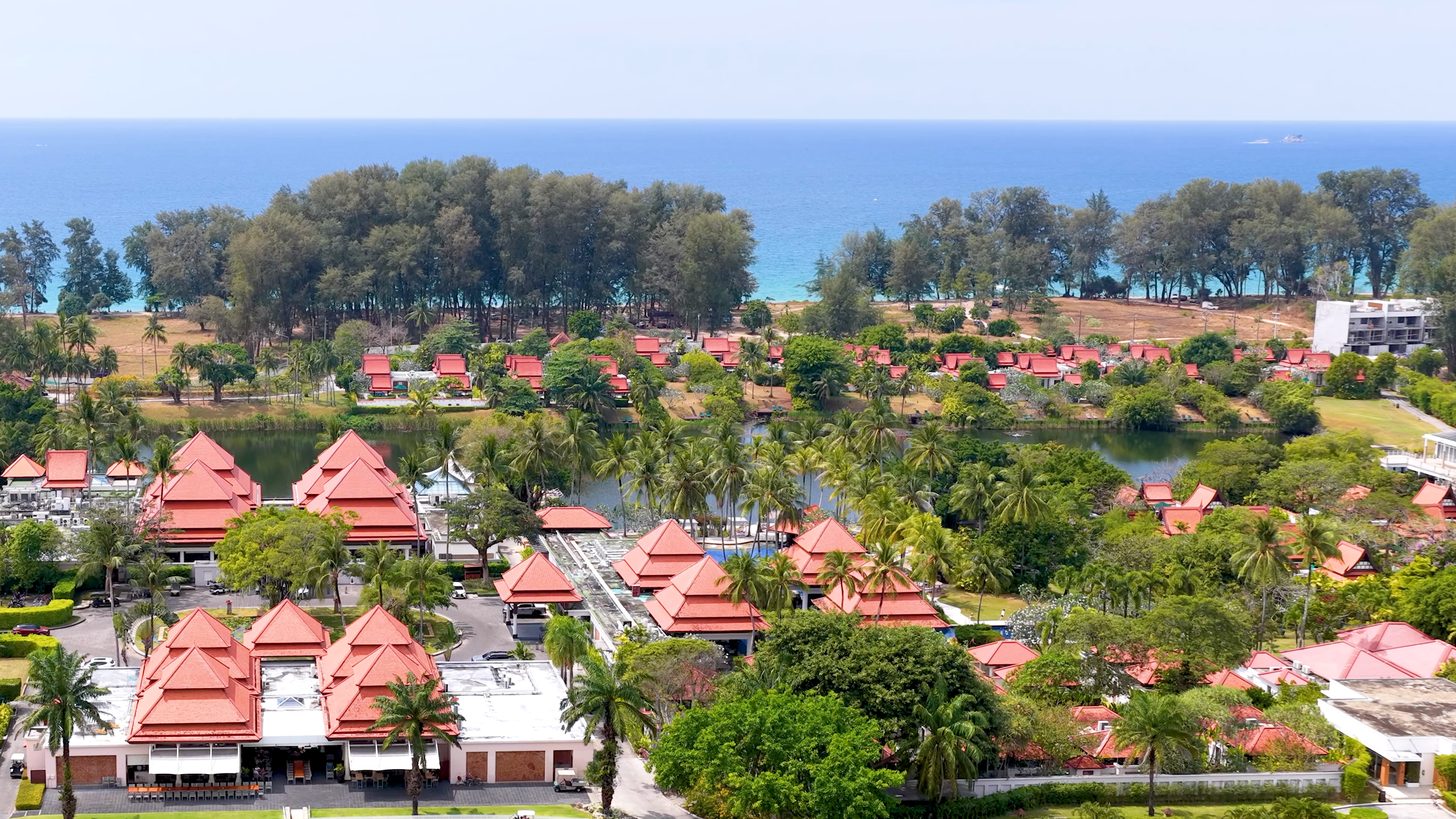 Aerial view of a resort in Phuket with red roofs among palm trees and the sea on the horizon