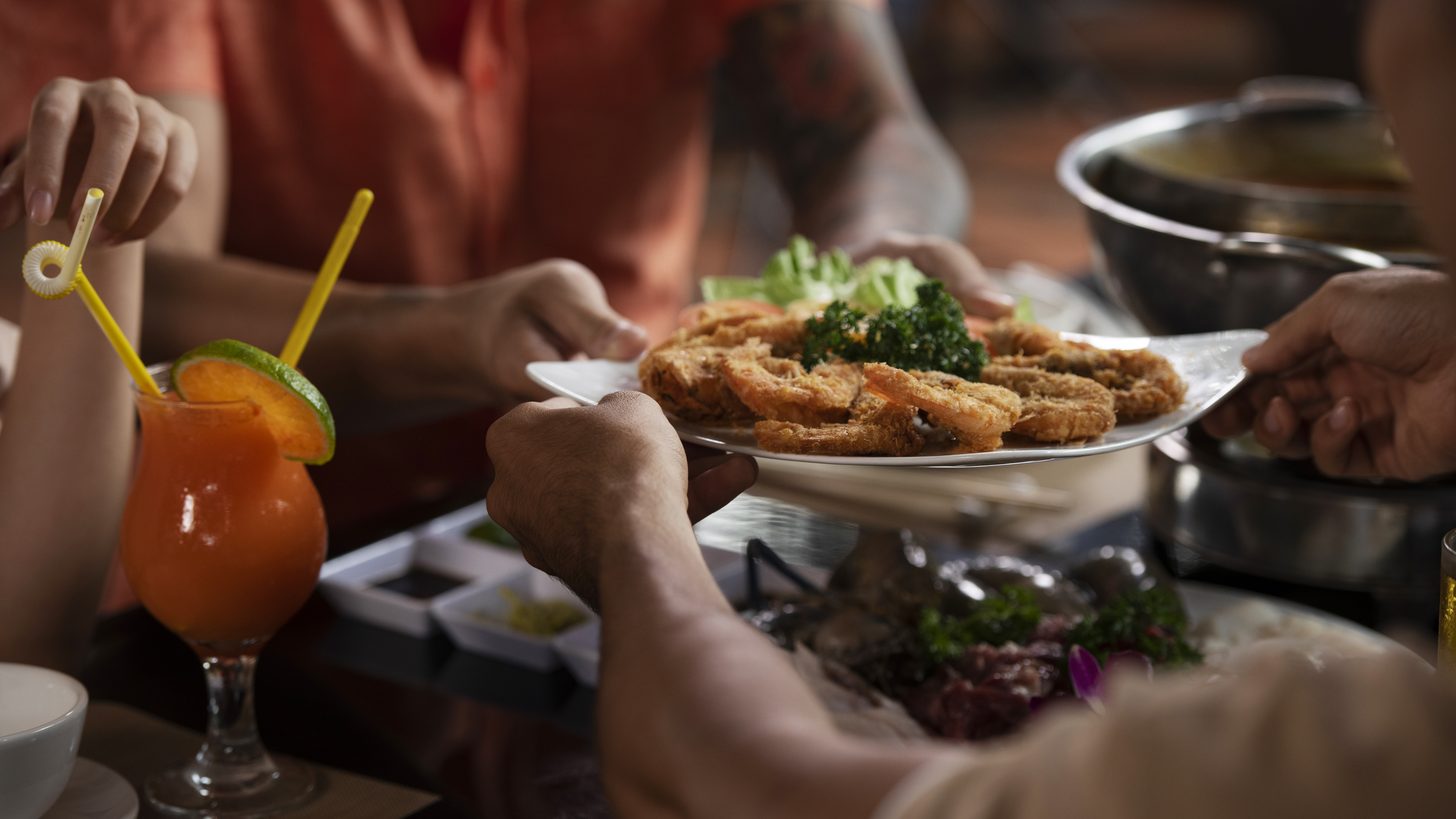 Hands passing a plate of fried food across a table at a shared group dinner