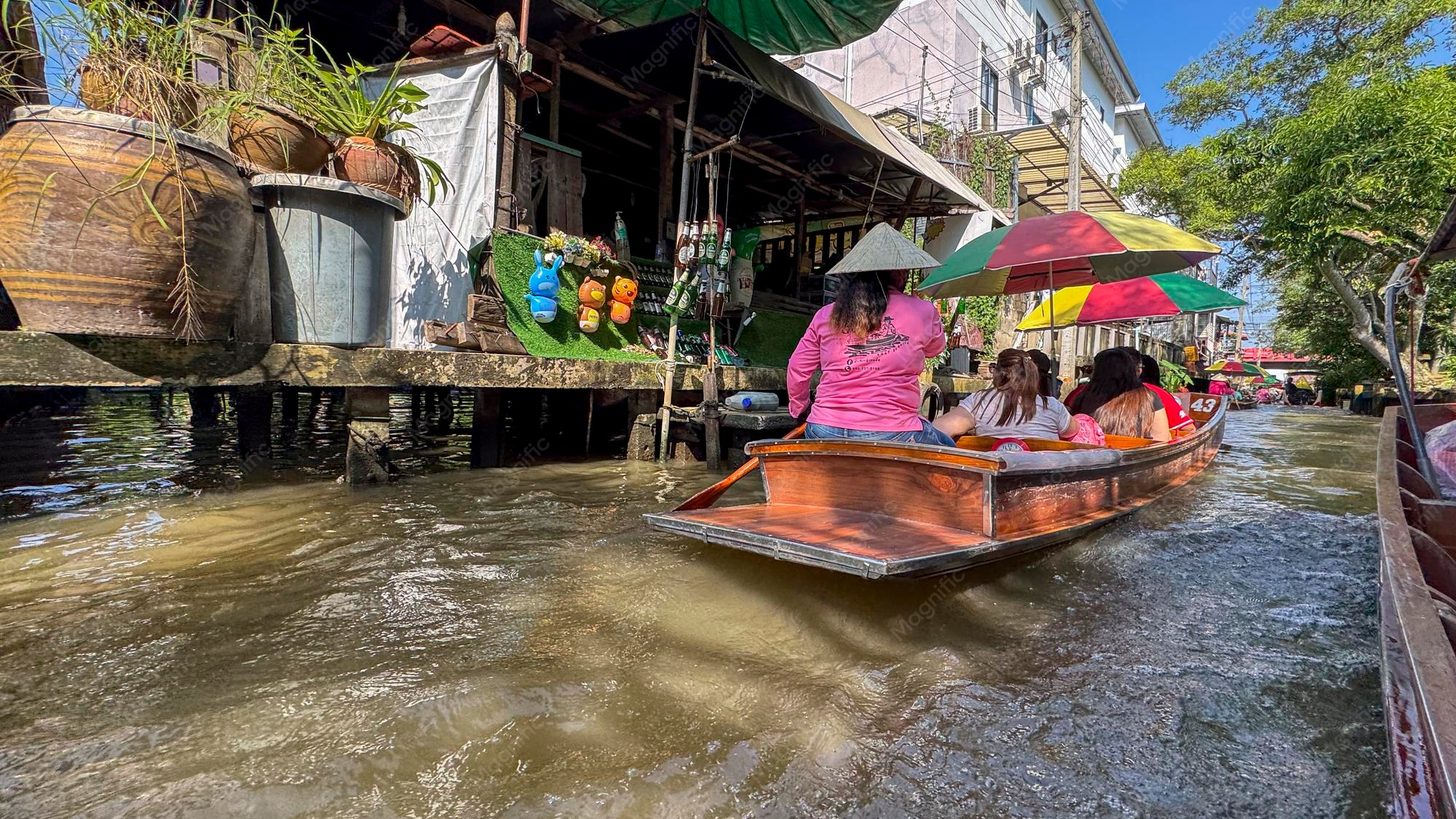 Wooden boats carrying visitors along a canal lined with waterside houses near Bangkok