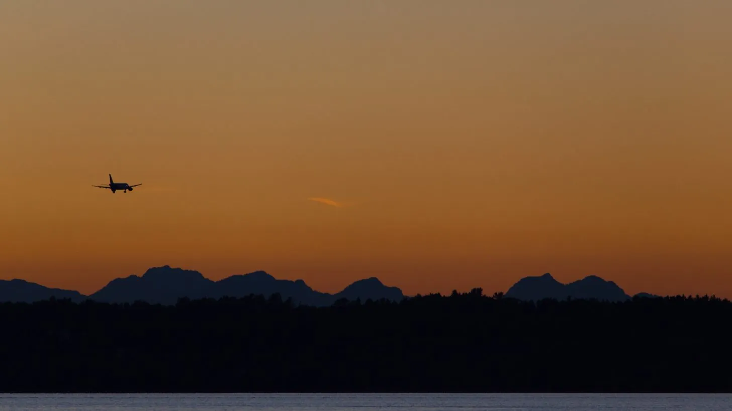Ein Flugzeug als Silhouette vor orangem Abendhimmel über einem dunklen Hügelkamm