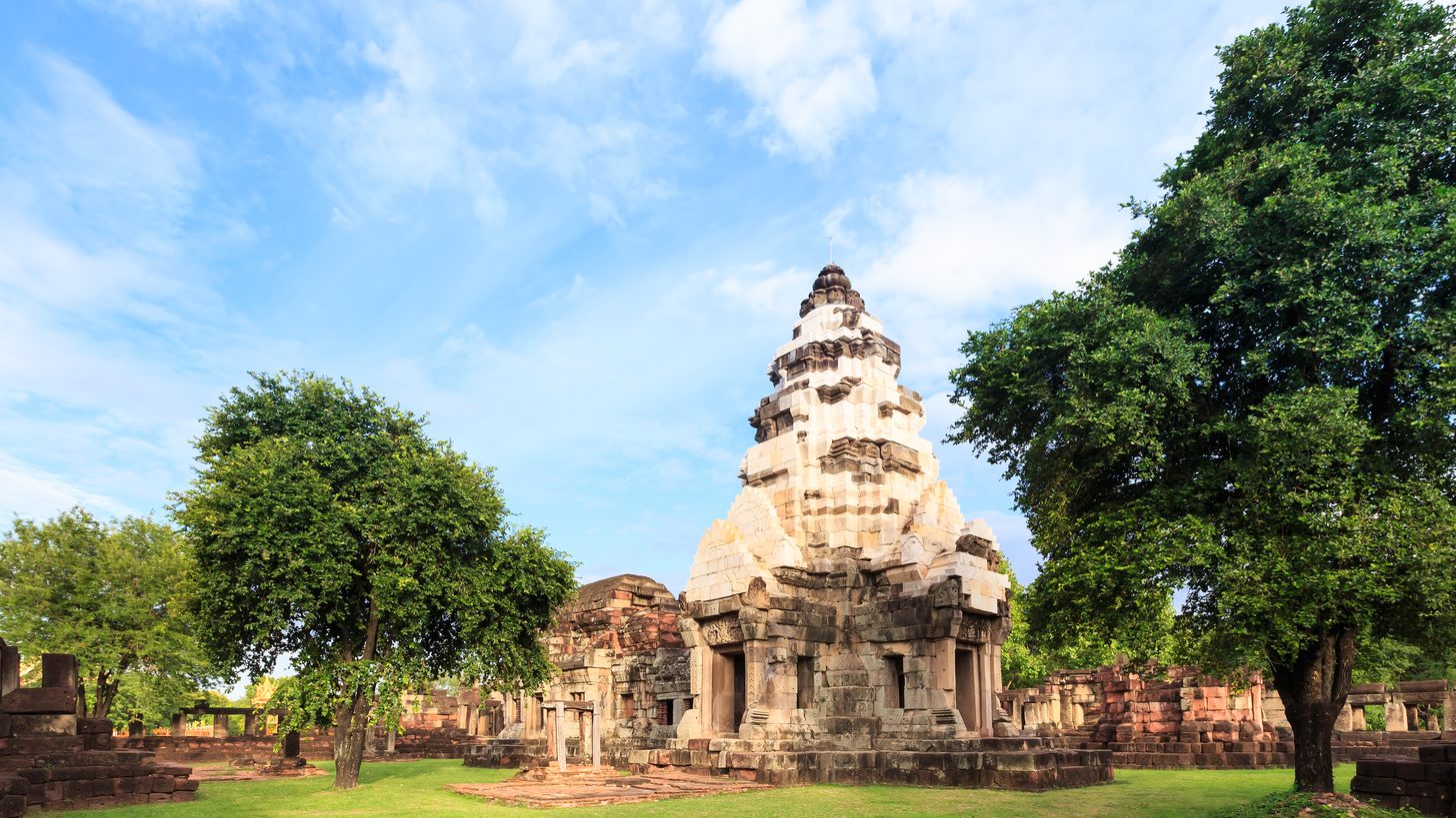 The sandstone tower of a Khmer-era sanctuary against a blue sky, framed by trees