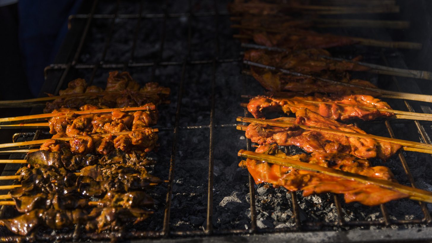 Chicken and pork skewers grilling over charcoal at a Thai street food stall