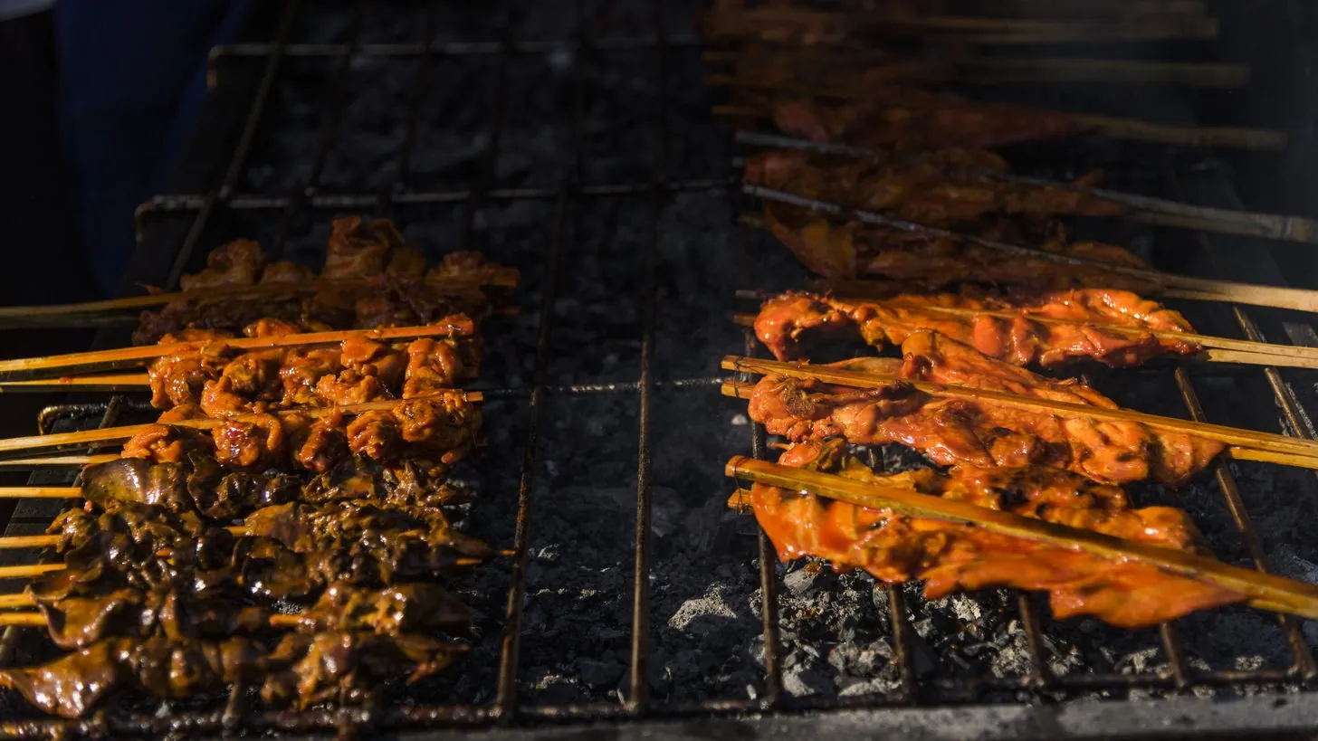 Hähnchen- und Schweinefleischspieße auf dem Holzkohlegrill eines thailändischen Straßenstands