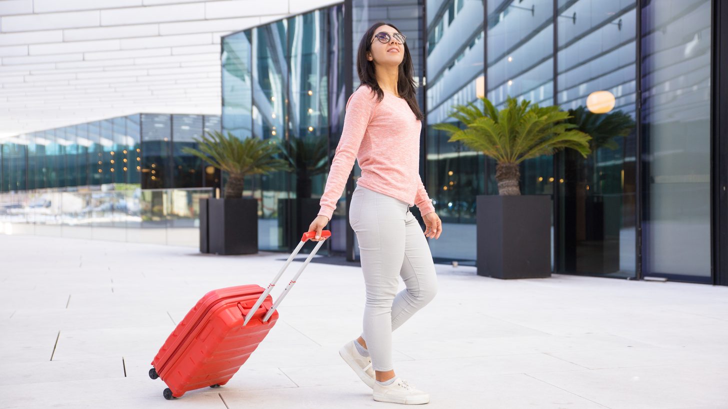 A traveller in sunglasses pulling a red suitcase out of a glass-fronted airport building