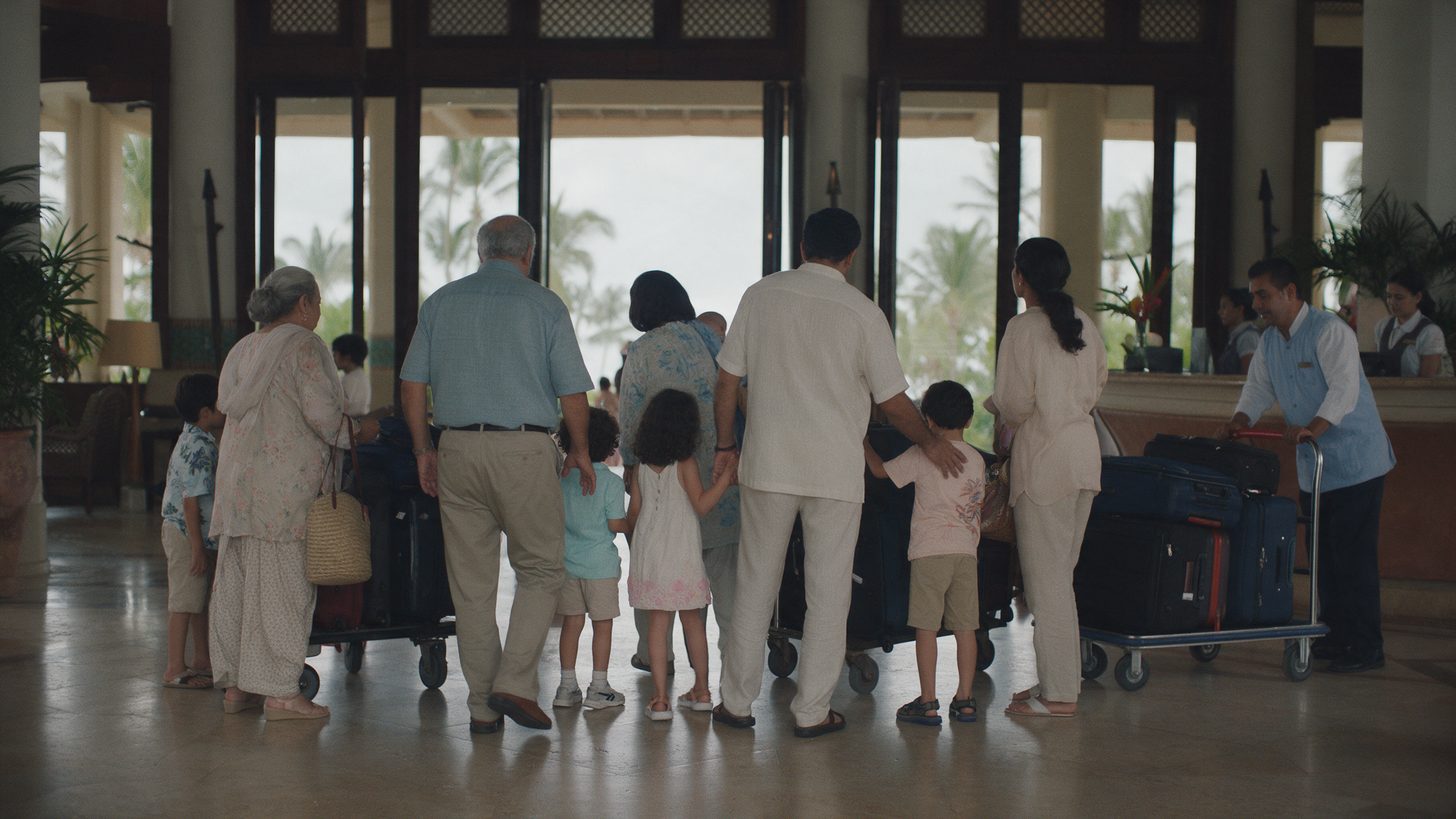 A large family with luggage trolleys at a hotel reception desk, seen from behind