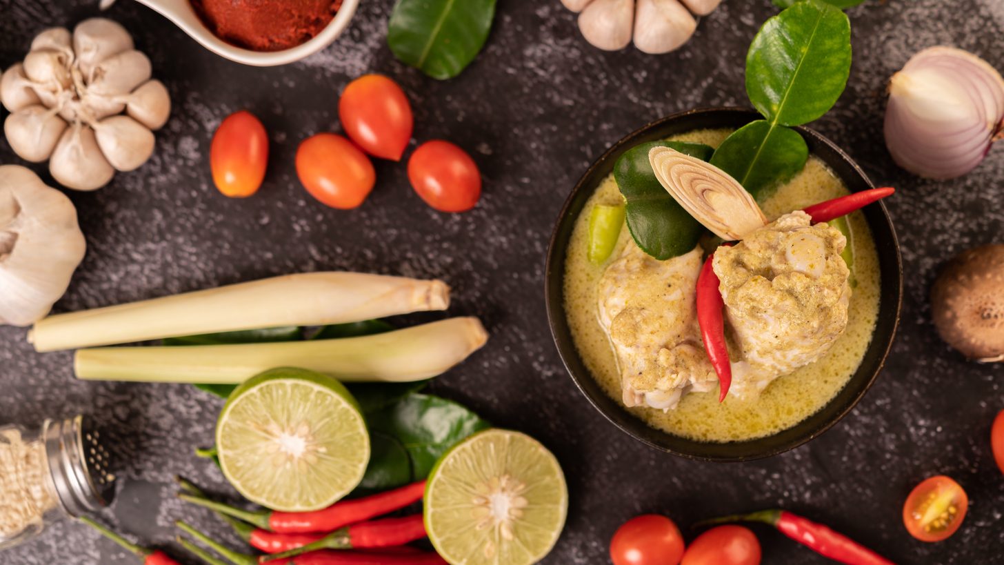 Un cuenco de curry verde con pollo, guindilla y albahaca junto a lima, hojas de lima kaffir y ajo