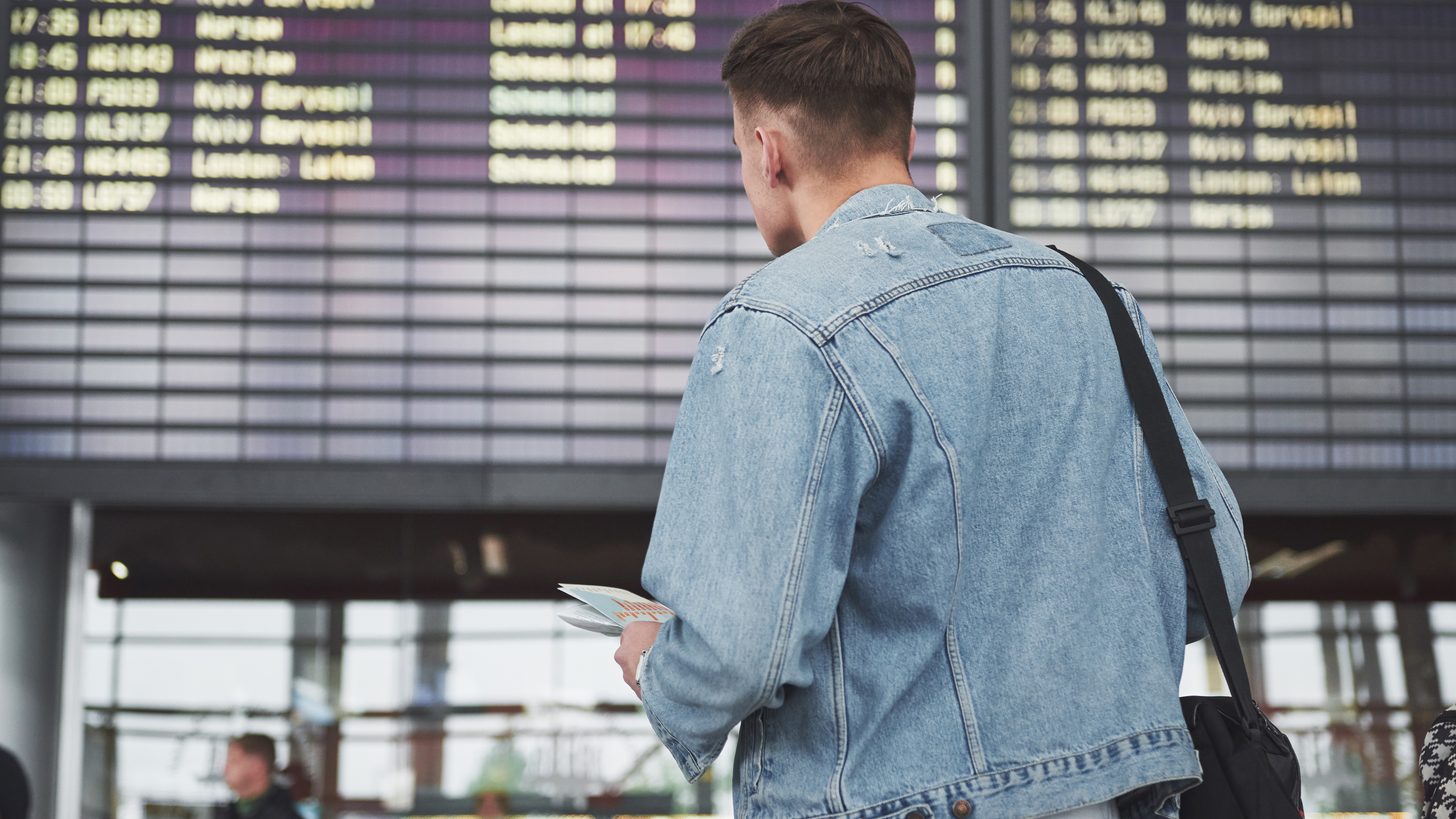 Un passager, billet en main, consulte le tableau des départs d'un aéroport