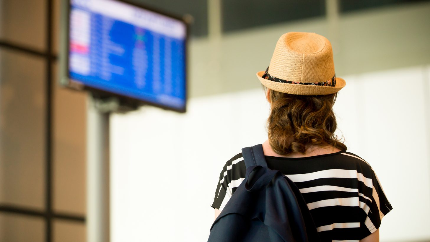 Une voyageuse en chapeau de paille regarde un écran d'information des vols