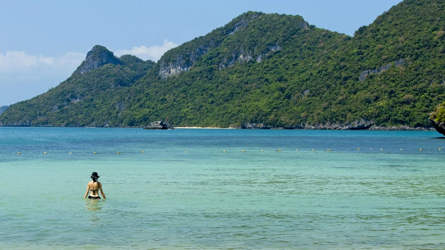 Una bañista en aguas claras frente a una isla boscosa del Parque Nacional Marino de Ang Thong