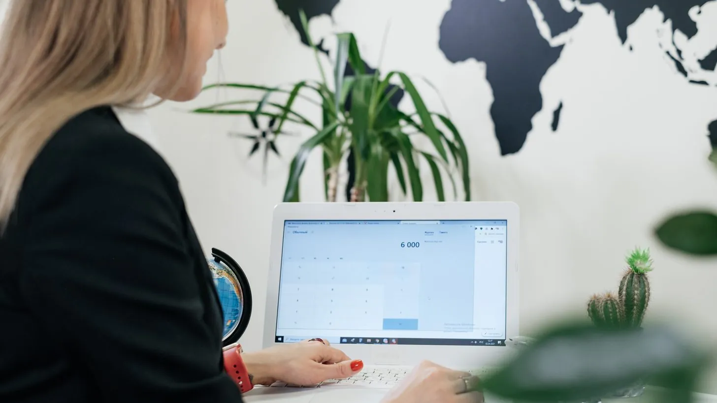 A travel agent working at a laptop in an office, a world map on the wall behind