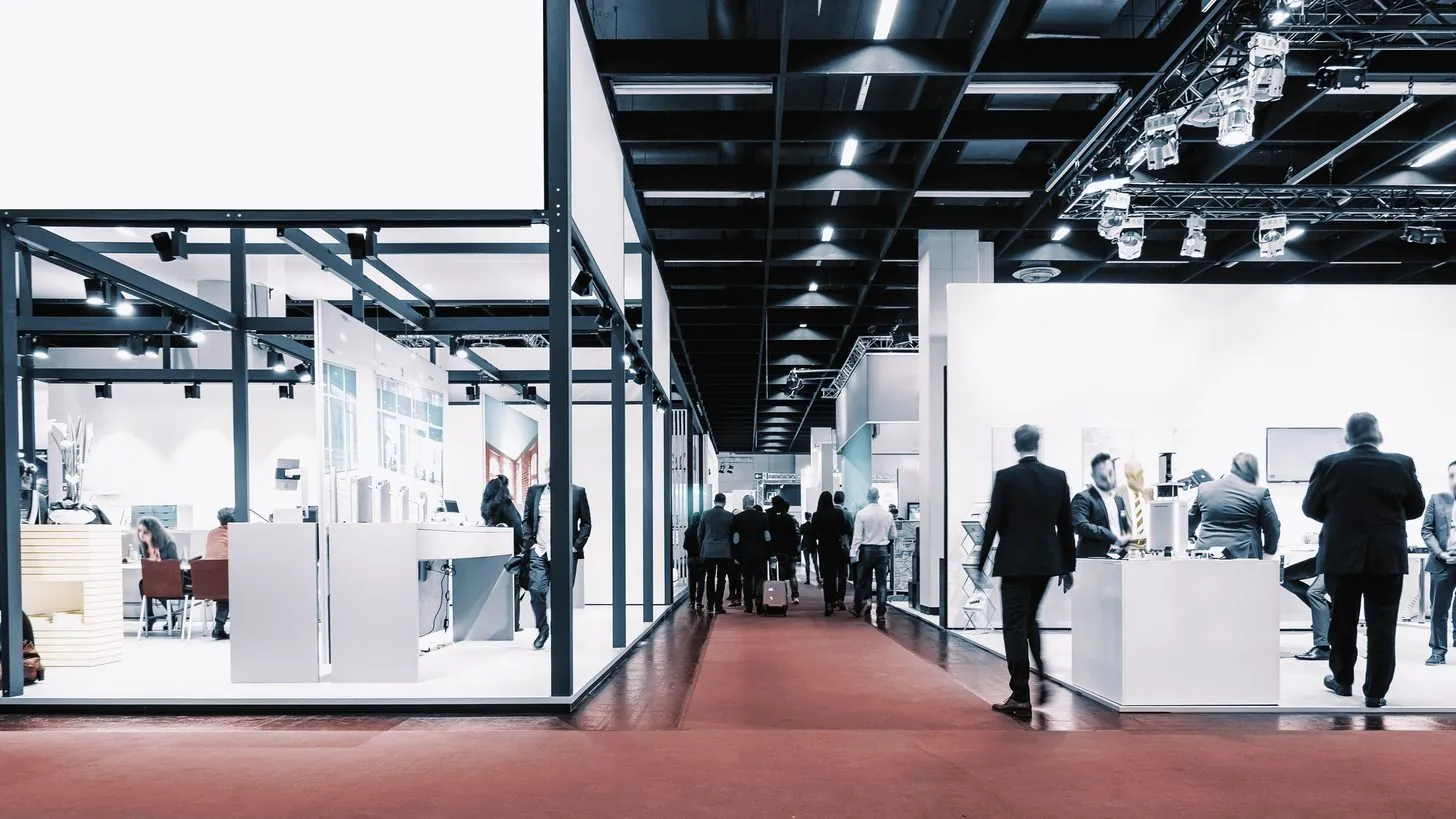 Visiteurs en tenue d'affaires marchant dans une allée moquettée entre les stands d'un salon professionnel