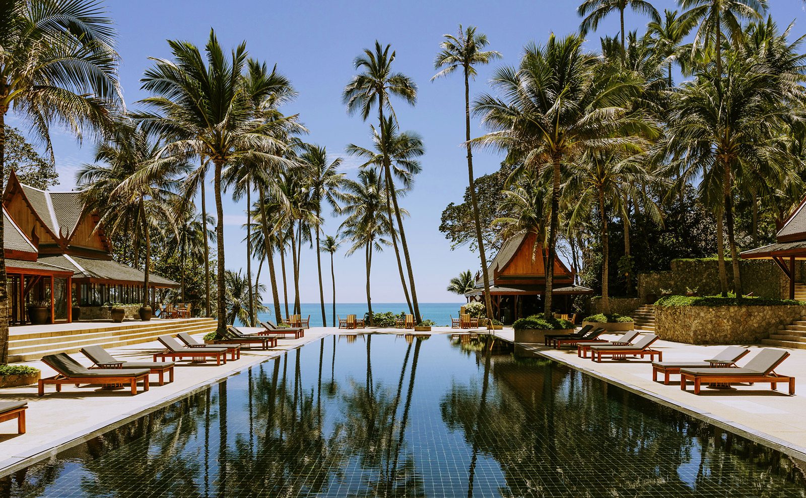 Main pool at Amanpuri, Phuket, lined with sun loungers and coconut palms, with pavilions on either side