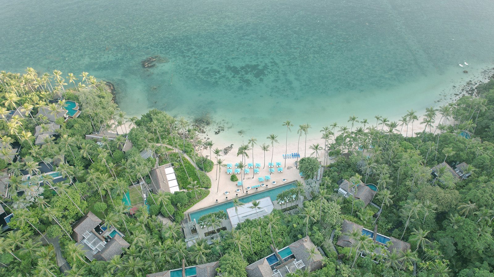 Aerial view of Four Seasons Resort Koh Samui, with villas on the forested hillside above the beach and cove