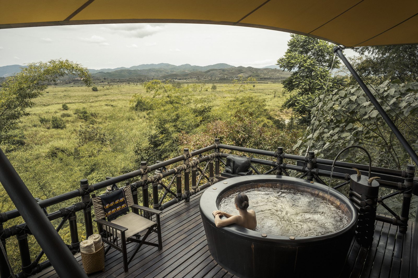 Guest in an outdoor tub on a tent veranda overlooking the valley at Four Seasons Tented Camp Golden Triangle